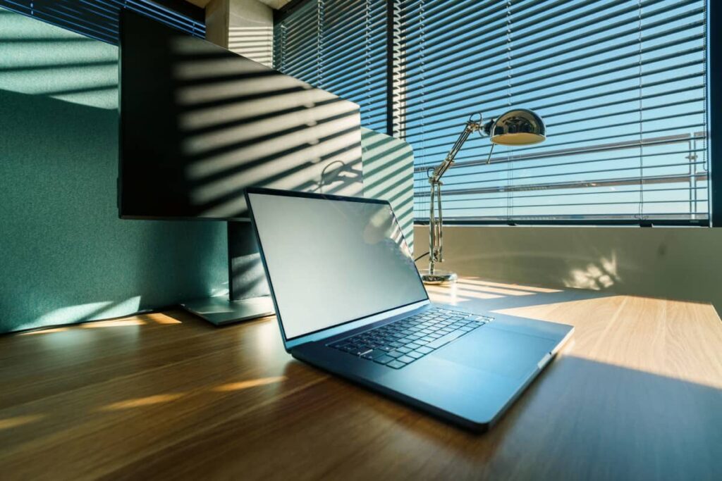 lato w biurze – przegrzane stanowisko pracy w mocnym świetle Laptop na biurku oświetlonym intensywnym, letnim słońcem – upał w biurze bez klimatyzacji
