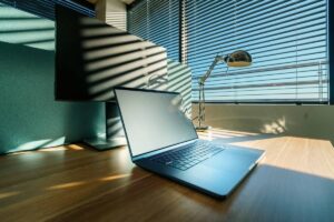 Laptop na biurku oświetlonym intensywnym, letnim słońcem – upał w biurze bez klimatyzacji