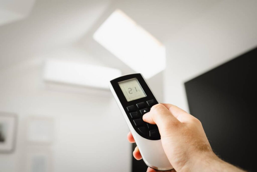 Upał w biurze bez klimatyzacji. Jak przetrwać lato za biurkiem i zachować energię? Ręka trzymająca pilot do klimatyzacji ustawiony na 21 stopni w biurze